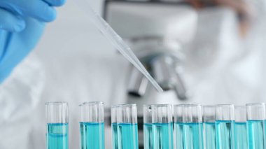 Mavi çözeltiyi içeren bilimsel cam kaplama, araştırmacı steril laboratuvar ortamında mikroskop yakınındaki pipetle sıvıyı dikkatlice dağıtıyor, kapatın. Tıp, sağlık ve bilim konsepti.
