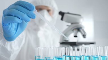 Koruyucu giysi giyen bilim araştırmacısı laboratuarda tıbbi araştırma deneyi yaparken deney tüplerine sıvıyı dikkatlice yerleştiriyor. Tıp, sağlık ve bilim konsepti.