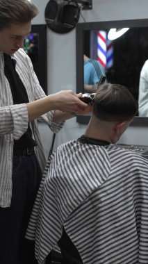 Profesyonel berber müşterilerin saçlarını elektrikli makasla dikkatlice buduyor, modern bir berber dükkanında şık ve kusursuz bir saç kesimi sağlıyor..