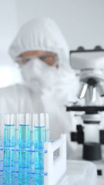 Koruyucu ekipman takan bilim araştırmacısı, tıbbi araştırma deneyi yaparken deney tüplerine sıvıyı dikkatlice yerleştiriyor. Tıp, sağlık ve bilim konsepti.