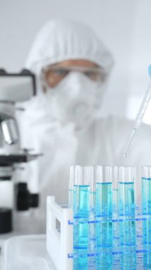 Koruyucu giysi giyen bilim araştırmacısı laboratuarda tıbbi araştırma deneyi yaparken deney tüplerine sıvıyı dikkatlice yerleştiriyor. Tıp, sağlık ve bilim konsepti.