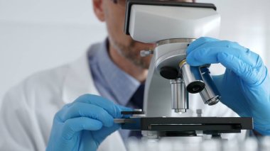 Beyaz önlüklü ve mavi eldivenli, mikroskop ayarlayan, modern laboratuarda ilaç araştırması yapan erkek bilim adamlarına yaklaş. Tıp ve bilim konsepti.