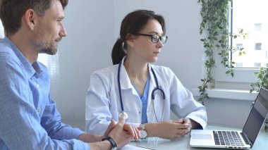 Bir erkek hastaya teşhis koyan kadın doktor muayenesi sırasında tıbbi tavsiye ve destek sunarak iletişim ve güveni teşvik ediyor. İlaç ve sağlık hizmetleri.