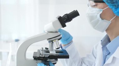 Araştırma örneğini mikroskop üzerinden inceleyen kadın bilim adamı tıbbi araştırma için koruyucu laboratuvar malzemesi giyiyor. Laboratuvar ve bilim konsepti.