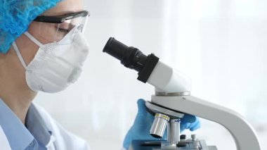Bir laboratuarda mikroskop kullanarak maske ve gözlük takan kadın bir bilim adamı araştırma ve bilimsel keşifte bulundu. Laboratuvar ve bilim konsepti.