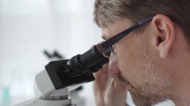 Bir erkek bilim adamının mikroskopla bakıp laboratuvar ortamında araştırma ve analiz yapması bilimsel araştırma ve keşifler sergilemesi. Tıp ve bilim konsepti.