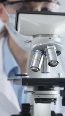 Bir laboratuarda mikroskop kullanarak maske ve gözlük takan kadın bir bilim adamı araştırma ve bilimsel keşifte bulundu. Laboratuvar ve bilim konsepti.