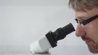 Bir erkek bilim adamının mikroskopla bakıp laboratuvar ortamında araştırma ve analiz yapması bilimsel araştırma ve keşifler sergilemesi. Tıp ve bilim konsepti.