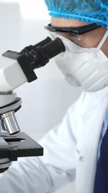 Erkek kıdemli bilim araştırmacısı örnek incelerken hassas mikroskobu kalibre ederek steril laboratuvar ortamındaki çığır açan tıbbi araştırmaları araştırıyor. Tıp ve bilim konsepti.