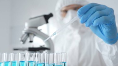 Koruyucu ekipman takan bilim araştırmacısı, tıbbi araştırma deneyi yaparken deney tüplerine sıvıyı dikkatlice yerleştiriyor. Tıp, sağlık ve bilim konsepti.