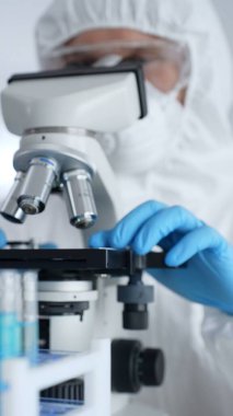 Koruyucu ekipman takan bilim araştırmacısı mikroskobu ayarlıyor, laboratuvar örneklerini steril araştırma ortamında hassasiyetle analiz ediyor. Tıp, sağlık ve bilim konsepti.