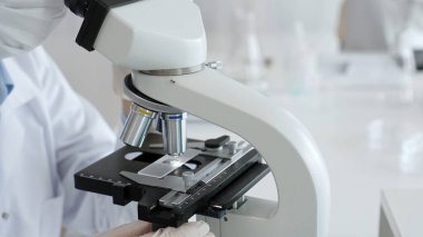 Bilim adamının beyaz eldivenli elleri parlak bir laboratuvarda mikroskobu ayarlıyor, kesinliği vurguluyor ve bilimsel araştırmalara odaklanıyor. Tıp, sağlık ve bilim konsepti.
