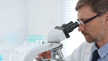 Bilimadamı mikroskobu inceliyor, gelişmiş laboratuvar ekipmanlarıyla tıbbi araştırmaları analiz ediyor, potansiyel ilaç buluşlarını geliştiriyor. Tıp, sağlık ve bilim konsepti