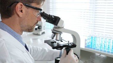 Korumalı giysiler giyerken bilimsel örnekleri analiz eden profesyonel bir araştırmacı, cam ekipmanlarla steril laboratuvar ortamında dikkatlice çalışıyor. Tıp, sağlık ve bilim konsepti