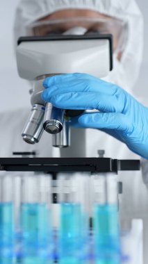 Mikroskop ayarlayan koruyucu ekipman takan bilimsel araştırmacı ya da virolog steril araştırma ortamında laboratuvar örneklerini hassasiyetle analiz ediyor. Tıp ve bilim konsepti.