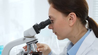 Kadın bilim adamı mikroskop örneklerini analiz ediyor, çağdaş laboratuvar ortamında gelişmiş ekipmanlarla tıbbi tedavileri araştırıyor. Tıp, sağlık ve bilim konsepti