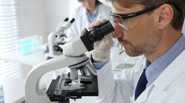 Korumalı giysiler giyerken bilimsel örnekleri analiz eden profesyonel bir araştırmacı, cam ekipmanlarla steril laboratuvar ortamında dikkatlice çalışıyor. Tıp, sağlık ve bilim konsepti