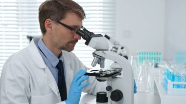 Gelişmiş laboratuvar araştırmaları sırasında mikroskopla biyolojik örnekleri inceleyen odaklanmış bir tıp bilimcisi. Tıp, sağlık ve bilim konsepti