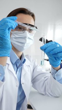 Bilimadamları laboratuvar tıbbi araştırma çalışmaları sırasında koruyucu giysi giyip tüpü hassas pipetle test etmek için kimyasal sıvı eklediler. Tıp, sağlık ve bilim konsepti