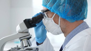 Koruyucu ekipman takan erkek bilim adamı mikroskop kaymasını inceliyor, steril laboratuvar ortamında araştırma örneklerini analiz ediyor, yakın plan. Tıp ve bilim konsepti.