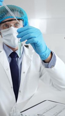 Steril laboratuvar çalışma alanı içindeki pipeti kullanarak turkuaz sıvı örneğini inceleyen koruyucu ekipman giyen bir bilim adamı. Tıp, sağlık ve bilim konsepti