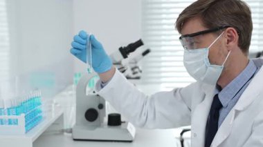 Koruyucu giysi giyen bilim araştırmacısı modern laboratuvar çalışma alanında mavi sıvı numunesini test tüpünden inceliyor. Tıp, sağlık ve bilim konsepti