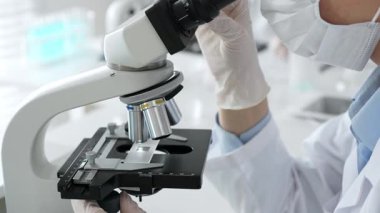 Beyaz koruyucu eldivenler giyen bilim teknisyeni laboratuvar mikroskobunu dikkatlice ayarlıyor ve titiz bir araştırma tekniği sergiliyor. Tıp, sağlık ve bilim konsepti