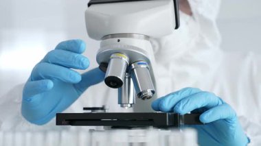 Laboratuvar araştırması sırasında mavi koruyucu eldiven takan bilim araştırmacısı ince ayar mikroskobu lensleri takıyor. Tıp, sağlık ve bilim konsepti.