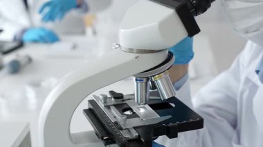 Mikroskop merceklerini inceleyen mavi koruyucu giysiler giyen, detaylı tıbbi laboratuvar araştırmaları yapan bilim adamlarına yaklaş. Tıp, sağlık ve bilim konsepti.