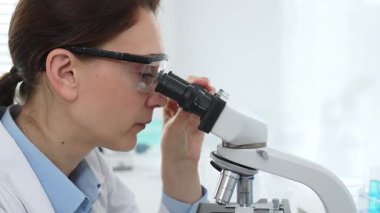 Kadın bilim adamı mikroskop örneklerini analiz ediyor, çağdaş laboratuvar ortamında gelişmiş ekipmanlarla tıbbi tedavileri araştırıyor. Tıp, sağlık ve bilim konsepti