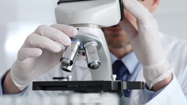 Beyaz koruyucu eldivenler giyen, laboratuvar mikroskobunu dikkatlice kalibre eden hassas tıbbi araştırma yapan erkek bilim araştırmacılarına yaklaş. Tıp ve bilim konsepti.