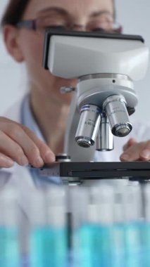 Kadın laboratuar bilimcisi mikroskop kayışını dikkatlice yerleştiriyor. Laboratuvarda araştırma hassasiyetini gösteriyor. Tıp, sağlık ve bilim konsepti.