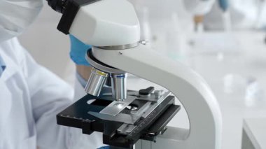 Mikroskop merceklerini inceleyen mavi koruyucu giysiler giyen, detaylı tıbbi laboratuvar araştırmaları yapan bilim adamlarına yaklaş. Tıp, sağlık ve bilim konsepti.