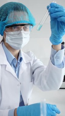 Steril laboratuvar ortamında tıbbi araştırma sırasında mikroskop yakınında mavi sıvı numunesini inceleyen koruyucu ekipman giyen bilim adamları. Tıp, sağlık ve bilim konsepti