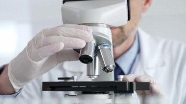 Beyaz koruyucu eldivenler giyen, laboratuvar mikroskobunu dikkatlice kalibre eden hassas tıbbi araştırma yapan erkek bilim araştırmacılarına yaklaş. Tıp ve bilim konsepti.