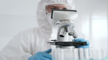 Koruyucu ekipman takan bilim araştırmacısı mikroskobu ayarlıyor, laboratuvar örneklerini steril araştırma ortamında hassasiyetle analiz ediyor. Tıp, sağlık ve bilim konsepti.