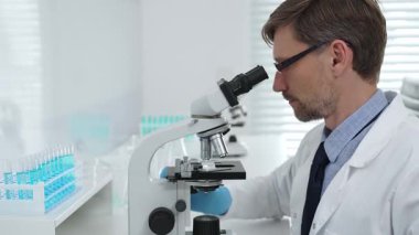 Gelişmiş laboratuvar araştırmaları sırasında mikroskopla biyolojik örnekleri inceleyen odaklanmış bir tıp bilimcisi. Tıp, sağlık ve bilim konsepti