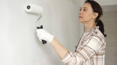 Profesyonel bir ressam koruyucu eldivenler giyerek duvarda pürüzsüz bir şekilde beyaz boya sürüyor, evin içini kusursuz bir fırça ve titiz bir boya tekniğiyle yeniliyor.