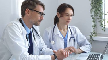 İki doktor bir dizüstü bilgisayardaki tıbbi kayıtları inceliyor, bir hastane veya klinik ortamdaki hasta verileri üzerine odaklanmış bir tartışmaya giriyorlar. İlaç ve sağlık hizmetleri kavramı.