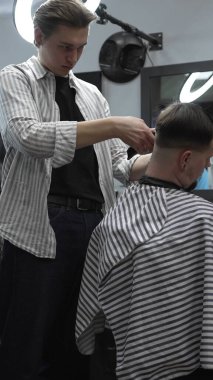 Profesyonel berber müşterilerin saçlarını elektrikli makasla dikkatlice buduyor, modern bir berber dükkanında şık ve kusursuz bir saç kesimi sağlıyor..