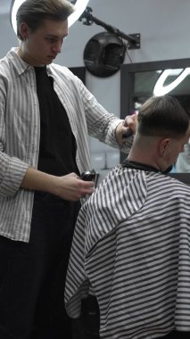 Profesyonel berber müşterilerin saçlarını elektrikli makasla dikkatlice buduyor, modern bir berber dükkanında şık ve kusursuz bir saç kesimi sağlıyor..