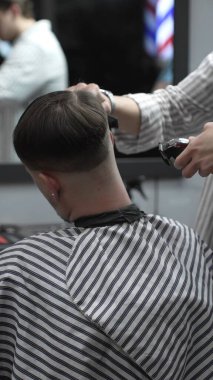 Profesyonel berber müşterilerin saçlarını elektrikli makasla dikkatlice buduyor, modern bir berber dükkanında şık ve kusursuz bir saç kesimi sağlıyor..