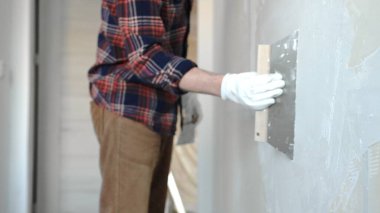 Eldiven takan ve işe odaklanan kimliği belirsiz erkek inşaat işçisi, sürmekte olan bir ev yenileme projesi sırasında duvara ustalıkla alçı yapıştırmak, yüzeyi düzleştirmek ve kapamak için mala kullanıyor.