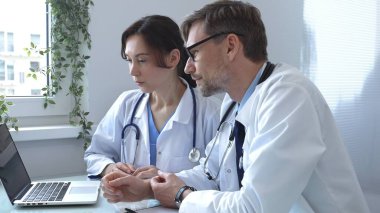 İki doktor bir dizüstü bilgisayarda tıbbi çizelgeleri inceliyor, hastane veya klinik ortamdaki hasta verilerini tartışıyorlar. Tıp ve sağlık hizmetleri kavramı