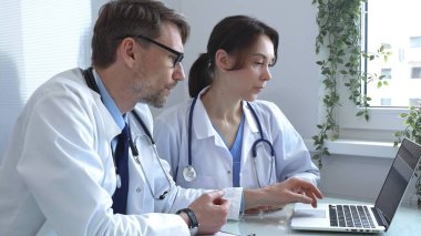 İki doktor bir dizüstü bilgisayarda tıbbi çizelgeleri inceliyor, hastane veya klinik ortamdaki hasta verilerini tartışıyorlar. Tıp ve sağlık hizmetleri kavramı