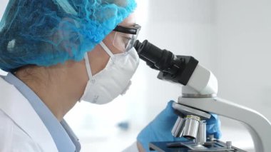 Bir laboratuarda mikroskop kullanarak maske ve gözlük takan kadın bir bilim adamı araştırma ve bilimsel keşifte bulundu. Laboratuvar ve bilim konsepti.