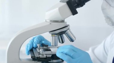 Mavi eldiven giyen bilim araştırmacısı mikroskop altında numuneleri dikkatlice analiz ederek hassas laboratuvar incelemesi yapıyor. Sağlık ve bilim konsepti.