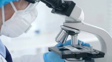 Laboratuvarda mikroskop ayarlayan mavi eldivenli erkek bilim adamlarına yakın çekim, bilimsel araştırma ve analiz yapıyorlar. Tıp ve bilim konsepti.