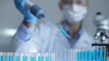 Laboratuvar ortamında test tüplerini mavi sıvıyla doldurmak için mikropipet kullanan kadın araştırmacı. Yakın çekim. Tıp ve bilim konsepti.