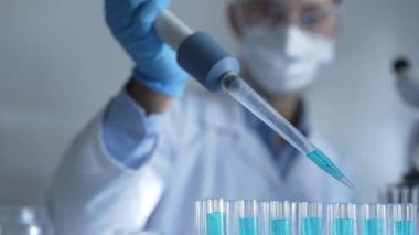 Laboratuvar ortamında test tüplerini mavi sıvıyla doldurmak için mikropipet kullanan kadın araştırmacı. Yakın çekim. Tıp ve Bilim.